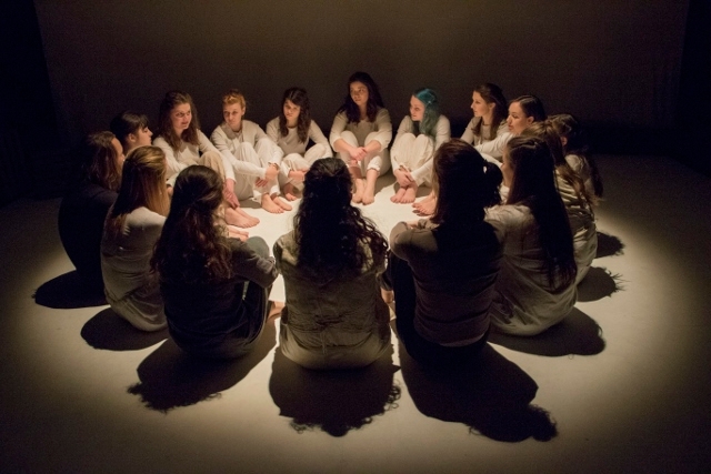 Actors sitting in a circle, backlit as part of their final presentation of "The Tempest"
